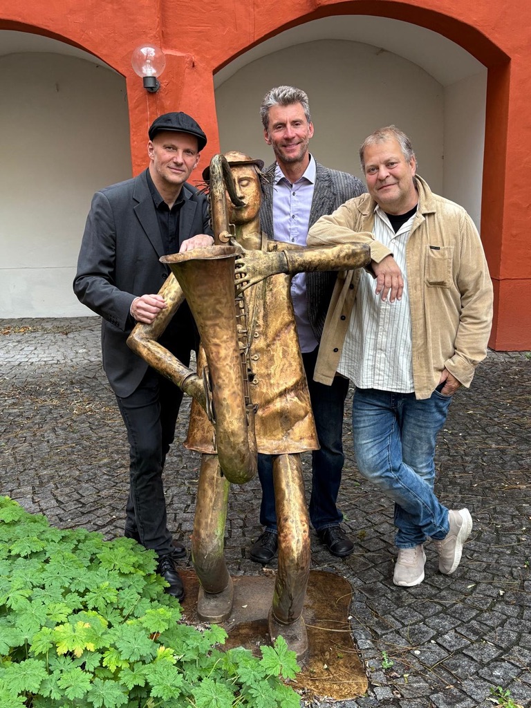 Drei Musiker mit einer Saxophon-Skulptur